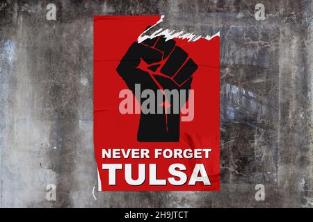 Full-frame weathered concrete wall with a torn red poster in the middle depicting a black fist with "Never forget Tulsa" written bellow. Stock Photo