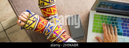 Above view of woman working and using laptop online computer writing with one hand. Mobile phone connection and brokes happy colorful socks on the sid Stock Photo