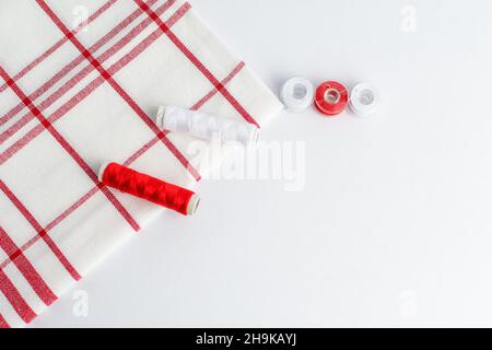 White and red spools of cotton thread prepared for sewing machine, near a textile cloth on a white table Stock Photo