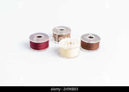 Different spools of mixed beige and brown cotton thread prepared for sewing machine, isolated on white, side view Stock Photo