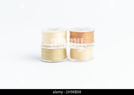 Different spools of mixed beige and brown cotton thread prepared for sewing machine, isolated on white, side view Stock Photo