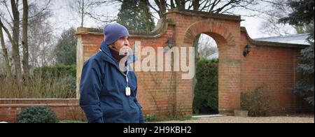 Old, elderly Asians. Elder Indian woman in her 80s walking outside in UK winter weather. Wearing a personal safety alarm Stock Photo