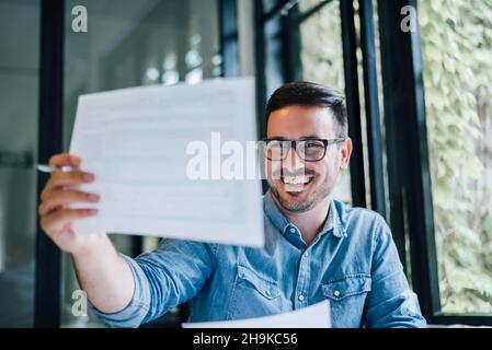 Portrait of young smiling cheerful man entrepreneur or businessman in casual office working with charts and graphs looking at paper documents accounti Stock Photo