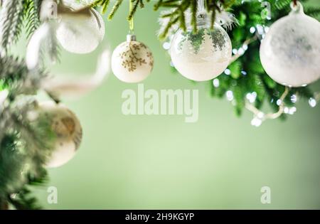 Christmas decoration with white christmas balls and fir tree branches against blurred green background, copy space for your product or text. Stock Photo