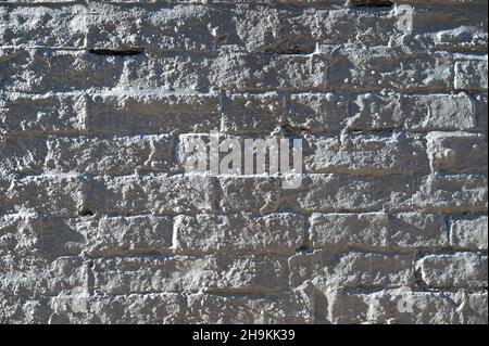 Abstract closeup of a white brick wall covered in a layer of concrete and side light revealing an uneven surface and textures. Stock Photo