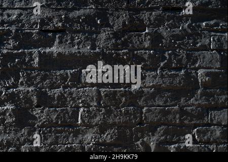 Abstract closeup of a dark brick wall covered in a layer of concrete and side light revealing an uneven surface and textures. Stock Photo