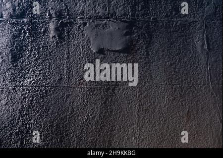 Abstract closeup of a dark block wall covered with concrete and side light revealing an uneven surface and textures. Stock Photo