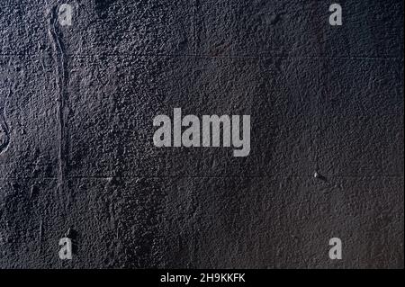Abstract closeup of a dark block wall covered with concrete and side light revealing an uneven surface and textures. Stock Photo