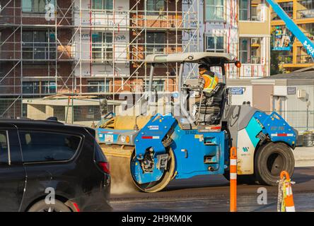 Tracked paver laying fresh asphalt pavement on top of the gravel base during road construction in the city. Stock Photo