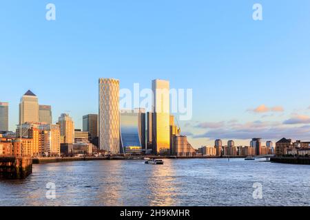 View down the River Thames, the evening sun illuminating Canary Wharf and the financial district, from the Thames Path at Limehouse, London, UK Stock Photo