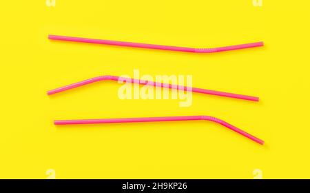 Three pink plastic drinking straws on yellow board, view from above Stock Photo