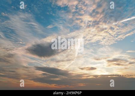 Morning blue orange sky, sun shining through clouds, some trails from airplanes visible Stock Photo