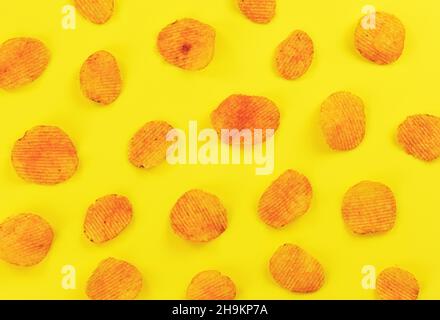 Potato crisps orange from paprika flavouring arranged on yellow board, view from above Stock Photo