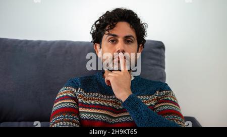 Handsome male model feels concerned puzzled lost in thoughts pondering making decision concept. Man wearing a winter sweater and thinking while sittin Stock Photo