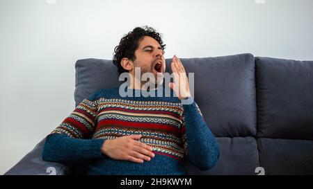 Adult man relaxing and yawing while sitting on couch home. Calm, carefree bearded man sits in a sofa and sleeps. A person is resting. Handsome male mo Stock Photo
