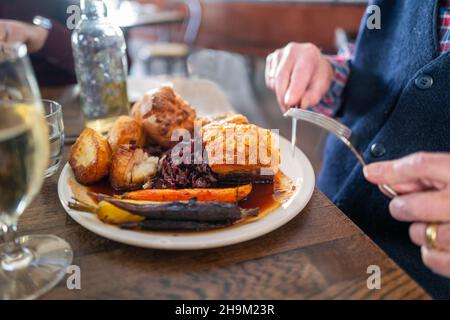 The golden thick crackling on top of roast pork belly on a white plate with roast potatoes and Yorkshire pudding with vegetables in a restaurant. A ma