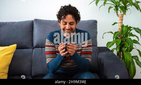 Portrait of happy man drinking morning expresso coffee while relaxing on couch and smiling. Cheerful caucasian guy having cafe and feeling confident i Stock Photo