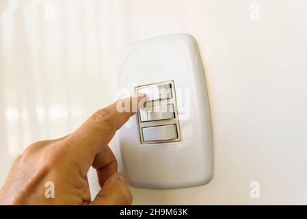 White electric switch on the wall. Hand turning on or off. Brazilian energy crisis. Stock Photo