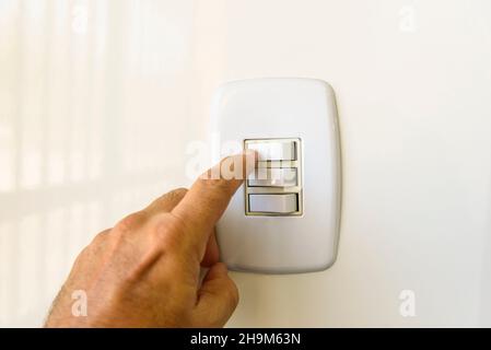 White electric switch on the wall. Hand turning on or off. Brazilian energy crisis. Stock Photo