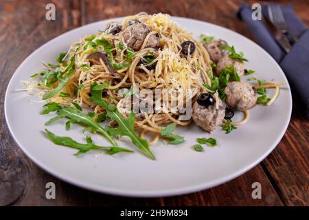 Spaghetti with meatballs, olives and arugula on wood table Stock Photo