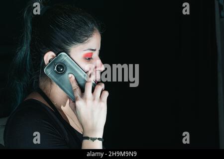 beautiful latina woman with green hair receiving a call, with her cell phone in her hand. with her eyes made up in red color and serious look. with a Stock Photo