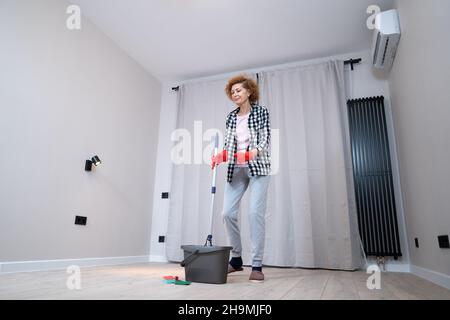 Jolly excited mature woman enjoying cleaning house, she dancing while washing floor. Happy elderly woman enjoying cleaning floors before moving to new Stock Photo