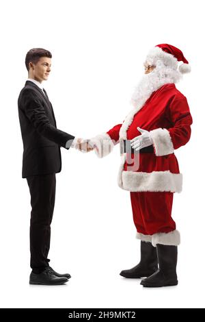 Full length profile shot of a young man in a suit and tie shaking hands with santa claus isolated on white background Stock Photo