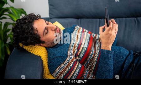 Depressed unhappy sad man using smartphone device while sitting on sofa at home. Mature man lying on couch reading messages on mobile phone. Caucasian Stock Photo