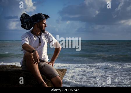 Young man with tropical hat sitting in beach chair drinking beer