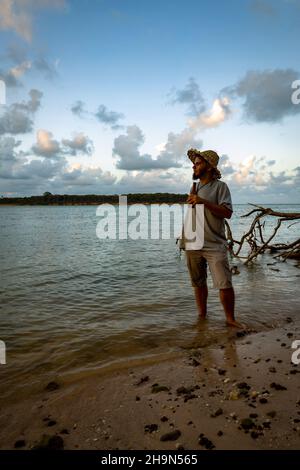Young age hippie traveler man in straw hat holding a bottle of beer during sunset on the edge of the lake. Stock Photo