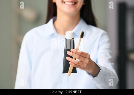 Woman with tube of black tooth paste and bamboo brush at home, closeup Stock Photo