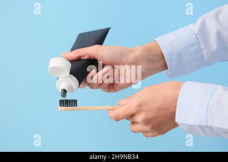 Woman applying black tooth paste onto bamboo brush on blue background, closeup Stock Photo