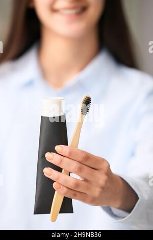 Woman with tube of black tooth paste and bamboo brush at home, closeup Stock Photo