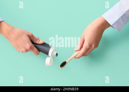 Woman applying black tooth paste onto bamboo brush on blue background, closeup Stock Photo