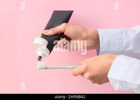 Woman applying black tooth paste onto plastic brush on pink background, closeup Stock Photo