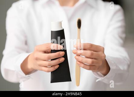 Woman with tube of black tooth paste and bamboo brush at home, closeup Stock Photo