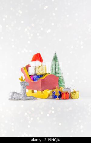 White glitter Christmas theme with Santa Clause sleigh with Christmas tree, silver reindeer, hat and gifts on white background with copyspace Stock Photo