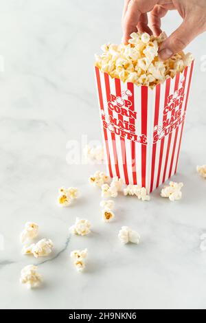 Someone taking a handful of popcorn from a popcorn carton. Stock Photo