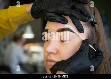 Experienced cosmetician pulling out brows. Removing eyebrows with hot wax. Stock Photo