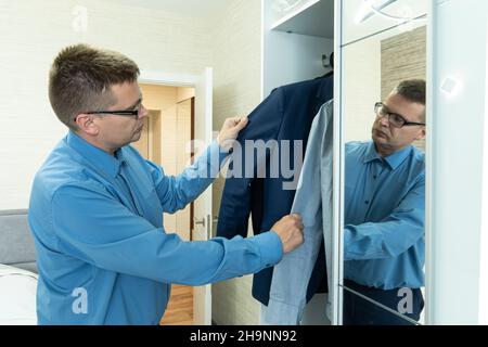 Young man businessman getting dressed for work. A young male businessman chooses a jacket. Dress code at work. Stock Photo