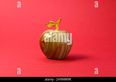 Souvenir from onyx or marble decorative miniature apple figure with golden branch and leaf on red background close up Stock Photo