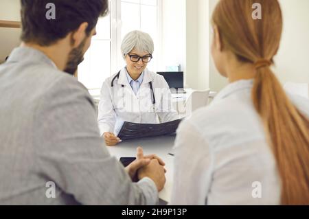 Mature female doctor in hospital advises expectant parents on planning pregnancy. Stock Photo