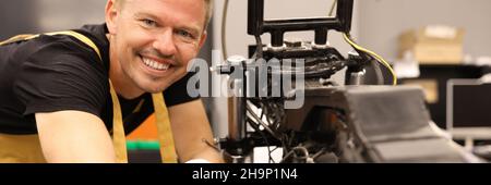 Smiling male locksmith repairing motorcycle with wrench in service center Stock Photo