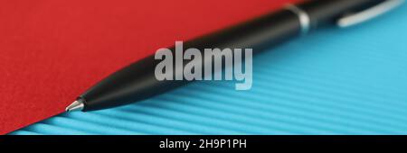 Black ballpoint pen lies on red blue background Stock Photo
