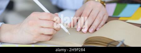 Woman holds in hand white pencil and notebook on desktop closeup Stock Photo