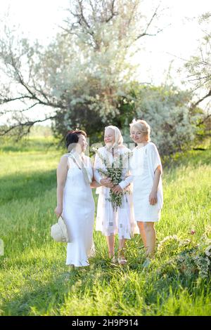 Happy daughters standing with old mother outside and wearing white dresses. Stock Photo