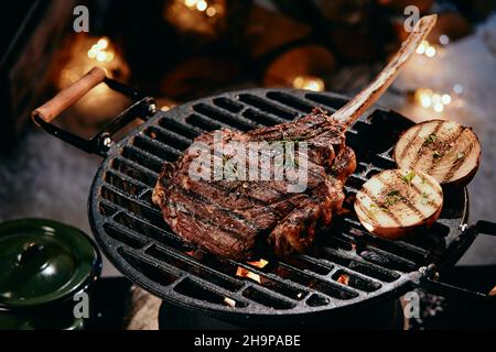 High angle of delicious hot Tomahawk steak and halves of onion preparing on grill rack in winter night Stock Photo