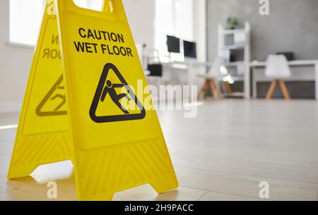Close up of yellow plastic standing safety sign warning us about wet slippery office floor. Stock Photo