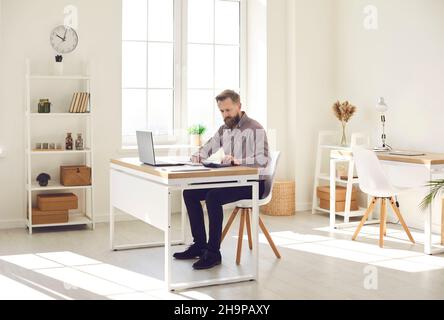 Man working in his office, sitting at desk with laptop computer and using calculator Stock Photo