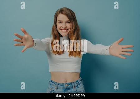 Young happy positive female in casual clothes spreading her arms wide in desire to welcome someone Stock Photo